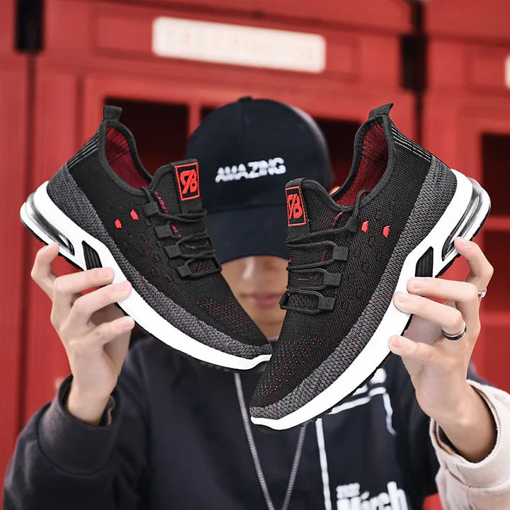 Person holding black and gray knit athletic shoes with white soles and red accents in front of red background