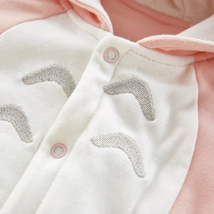 Close-up of baby onesie with pink snap buttons and gray embroidered eyebrows on white fabric