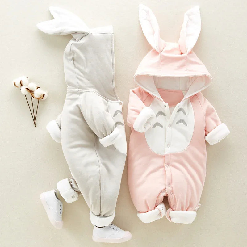 Pink and gray baby rompers with bunny ear hoods and white sneakers on a beige background