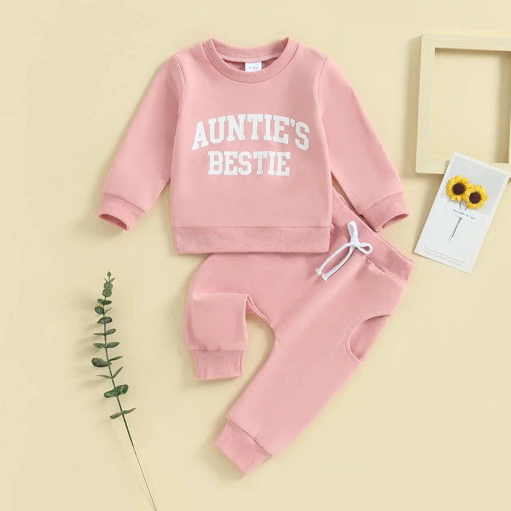 Pink baby outfit with sweatshirt reading 'Auntie's Bestie' and matching pants on beige background