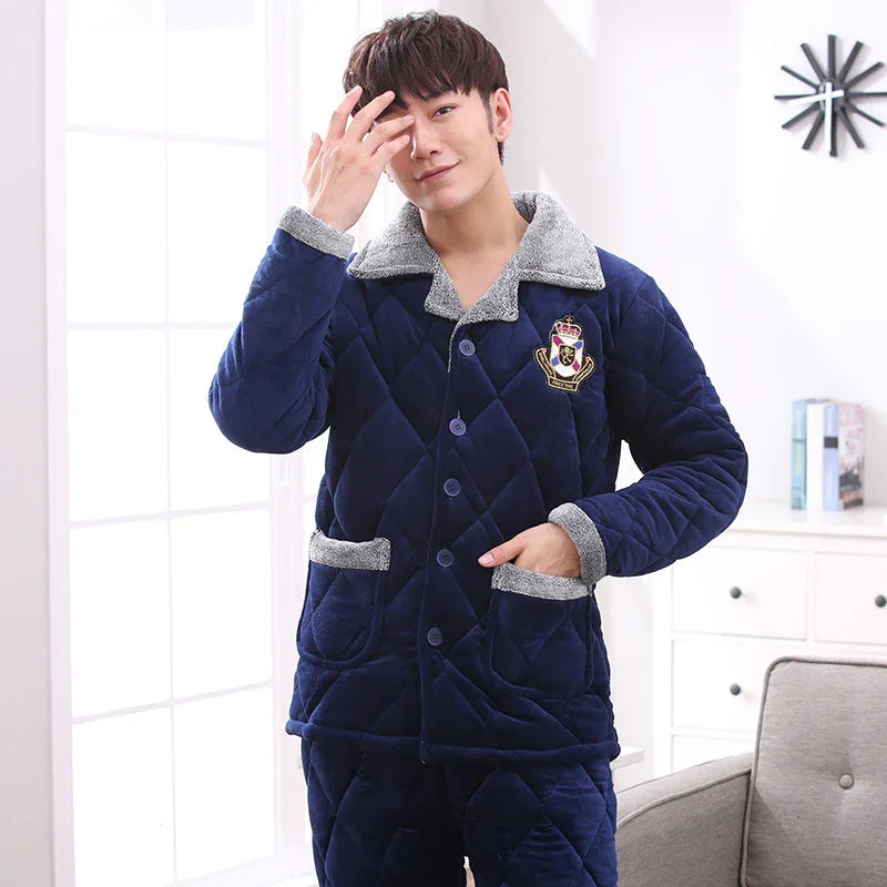 Man wearing navy blue quilted fleece pajama set with grey collar and cuffs inside a bright room