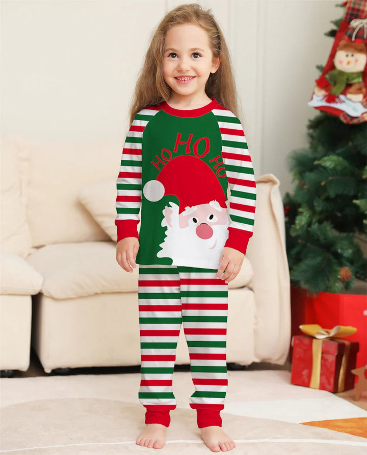 Smiling child wearing Christmas striped pajamas with Santa and Ho Ho Ho print in cozy living room