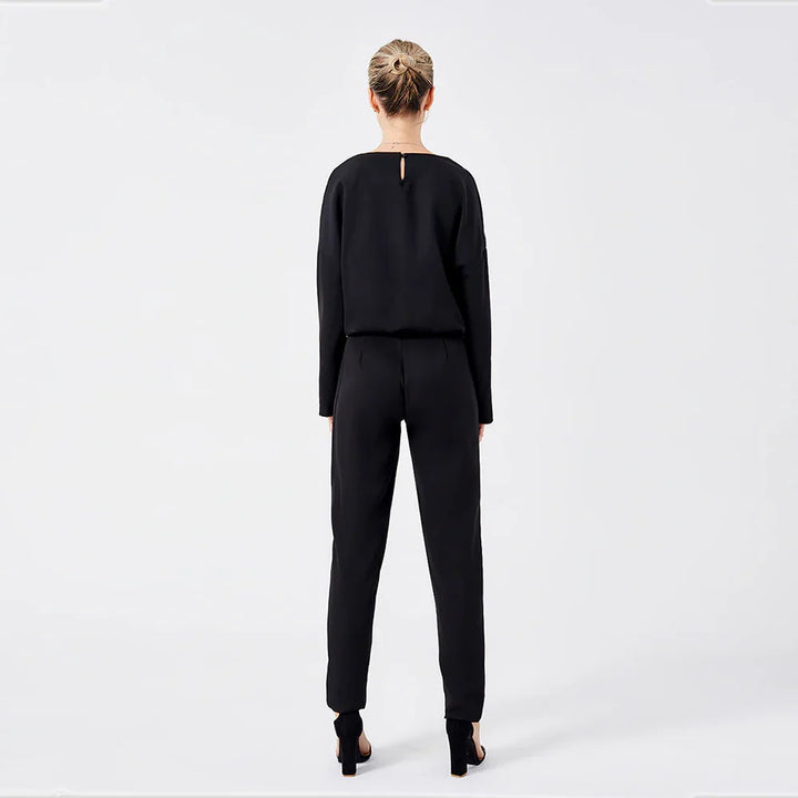 Woman wearing black long-sleeve top and pants with high-heeled sandals, standing against white background