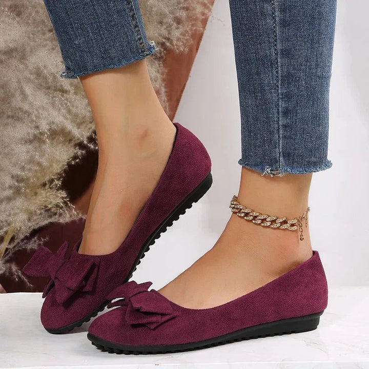 Woman wearing purple suede ballet flats with bow detail and gold anklet, paired with frayed hem blue jeans