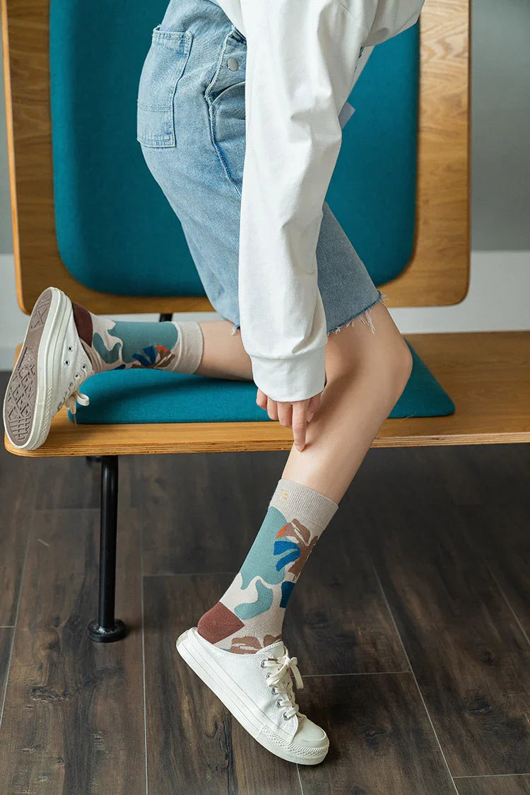 Person wearing colorful patterned socks and white sneakers sitting on blue and wooden bench with denim shorts