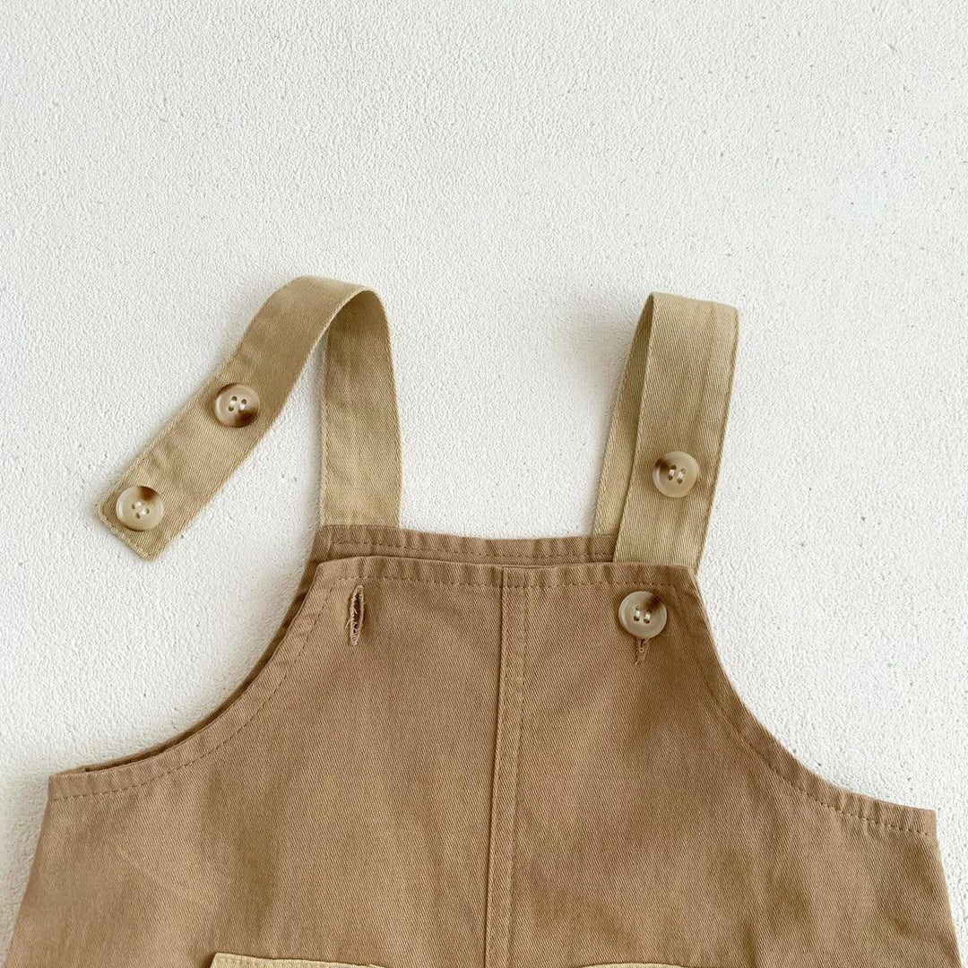 Close-up of beige cotton overalls with buttoned shoulder straps on white textured background