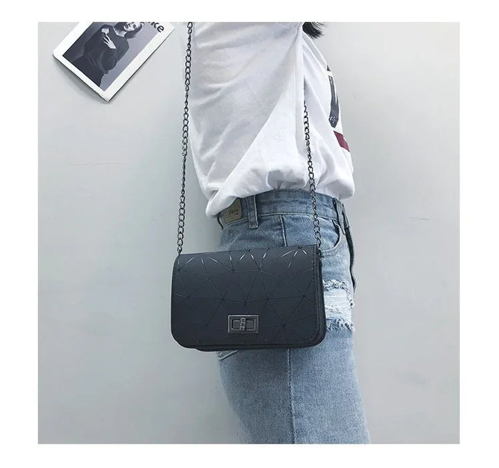 Black geometric quilted crossbody bag with chain strap worn over white t-shirt and distressed blue jeans