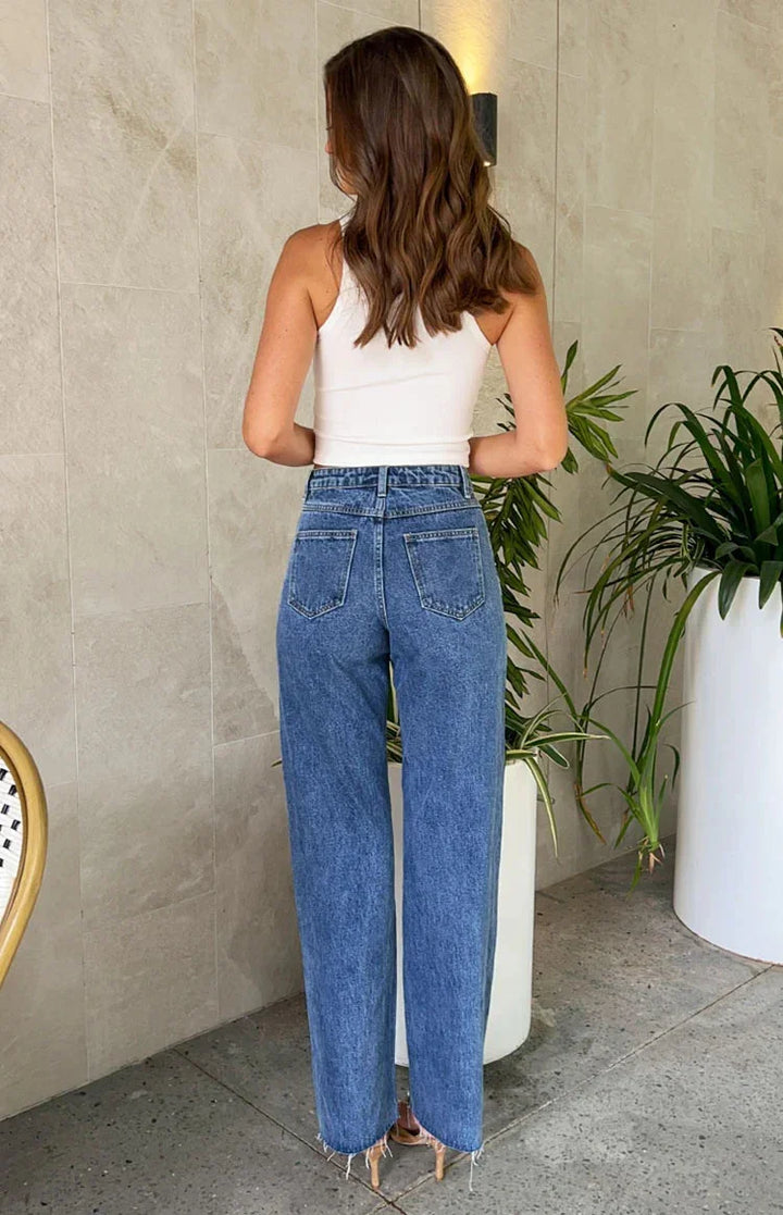 Woman with wavy hair wearing white crop top and high-waisted blue denim jeans in modern indoor space