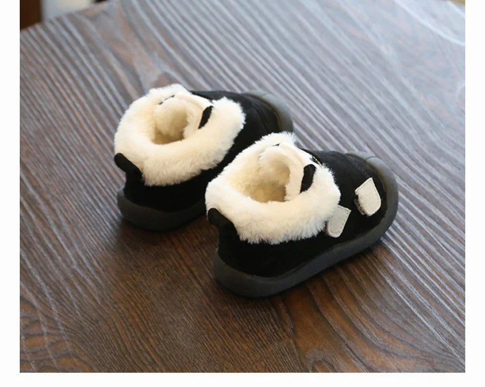 Black toddler shoes with white fluffy fur lining on wooden floor