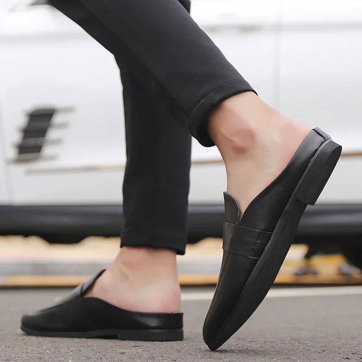 Close-up of black slip-on leather loafers worn with black pants on street background
