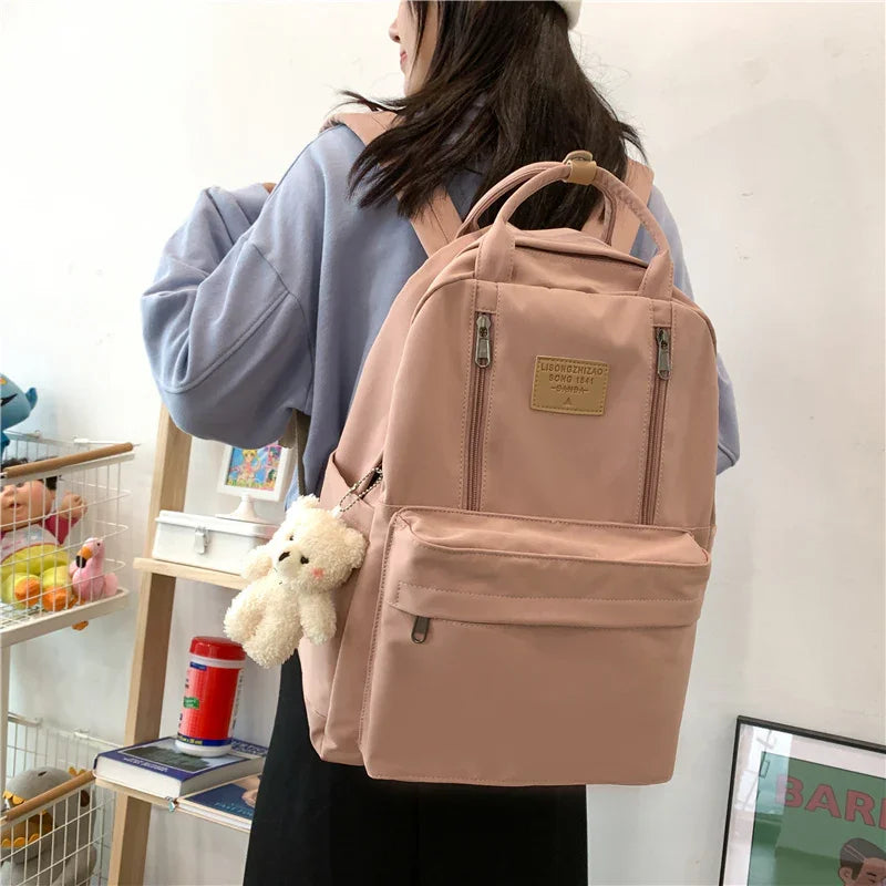 Woman wearing light purple sweatshirt with a pink backpack featuring multiple pockets and a small teddy bear keychain