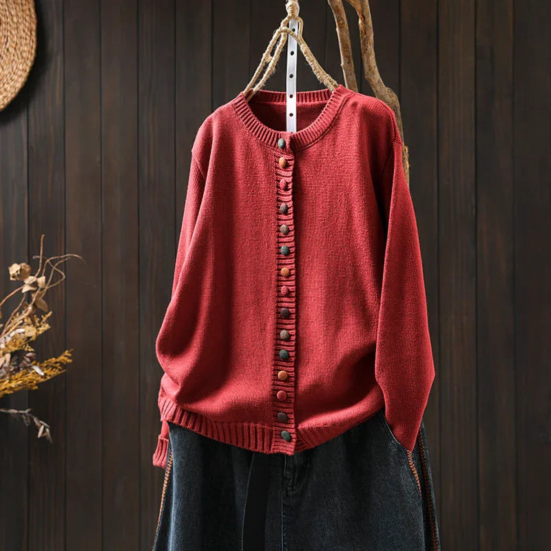 Red knitted cardigan with colorful buttons hanging on a rope hanger against dark wooden background