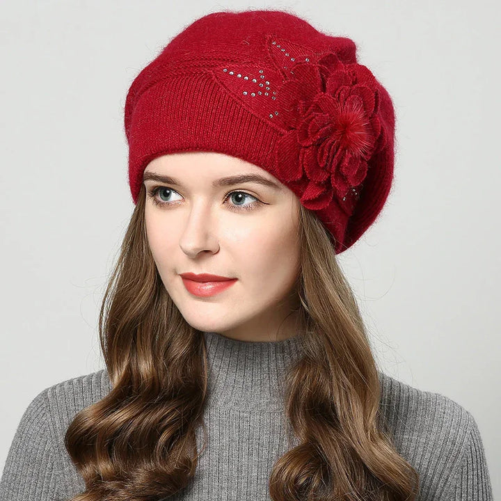 Woman wearing red knit beret with floral embellishment and rhinestones, gray ribbed sweater