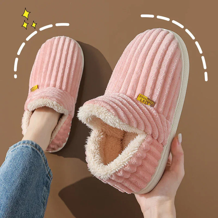 Pair of pink plush indoor slippers with soft fleece lining and ribbed design on brown background