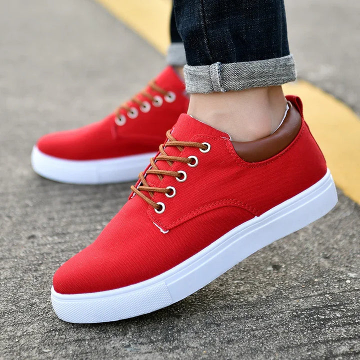 Close-up of casual red canvas sneakers with white soles and brown laces worn with rolled-up dark jeans on pavement