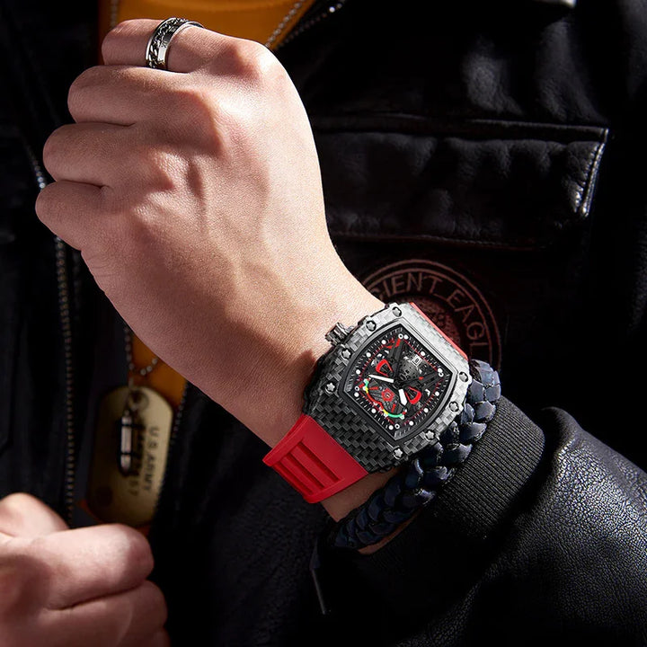 Mens wrist with black carbon fiber watch featuring red accents and red rubber strap, styled with braided bracelet