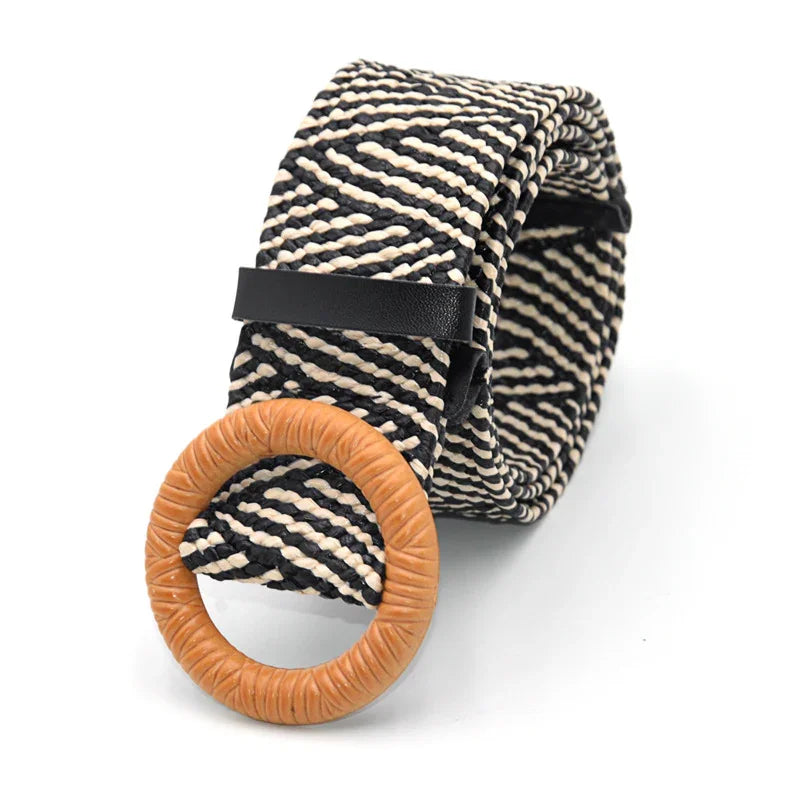 Black and white woven fabric belt with a round tan wooden buckle, coiled on white background