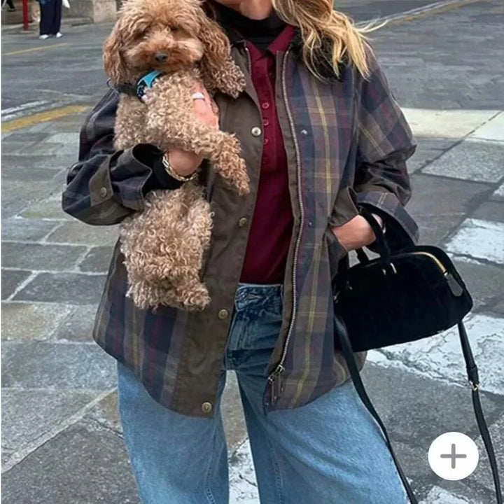 Person wearing plaid jacket and blue jeans holding curly brown dog on city street