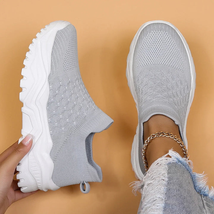 Light gray slip-on knit sneakers with chunky white soles on foot and held in hand