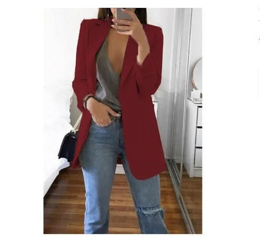 woman wearing red blazer, gray top, and ripped blue jeans taking mirror selfie in bedroom