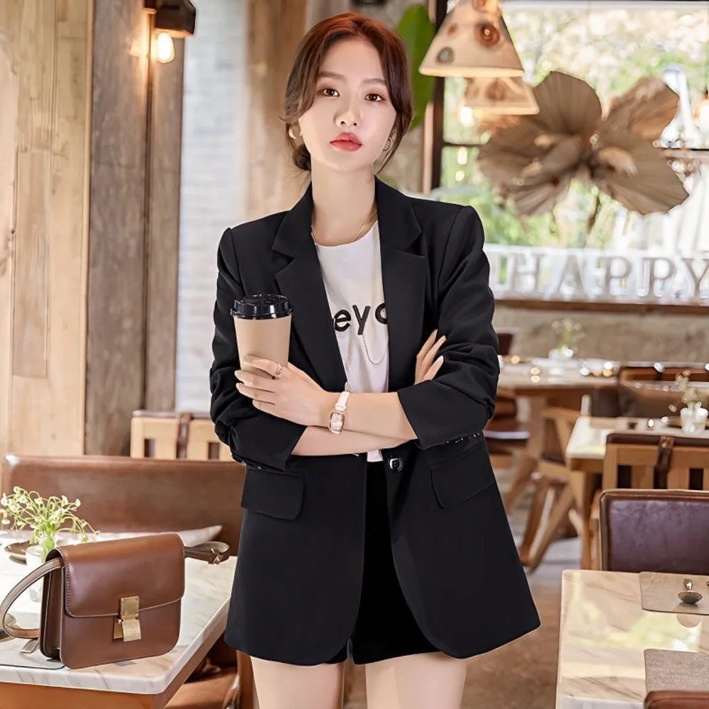 Stylish woman in black blazer and shorts holding coffee cup in cozy cafe setting with brown leather bag
