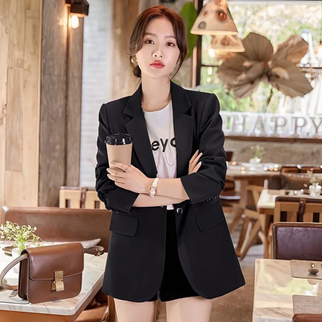 Stylish woman in black blazer and shorts holding coffee cup in cozy cafe setting with brown leather bag