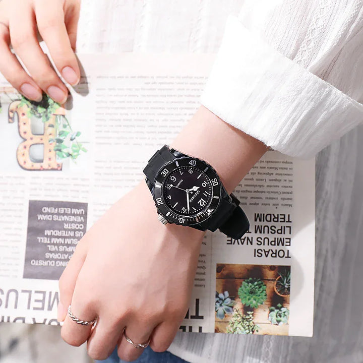 Black analog wristwatch with rotating bezel worn on wrist over white sleeve, holding a newspaper with plant images