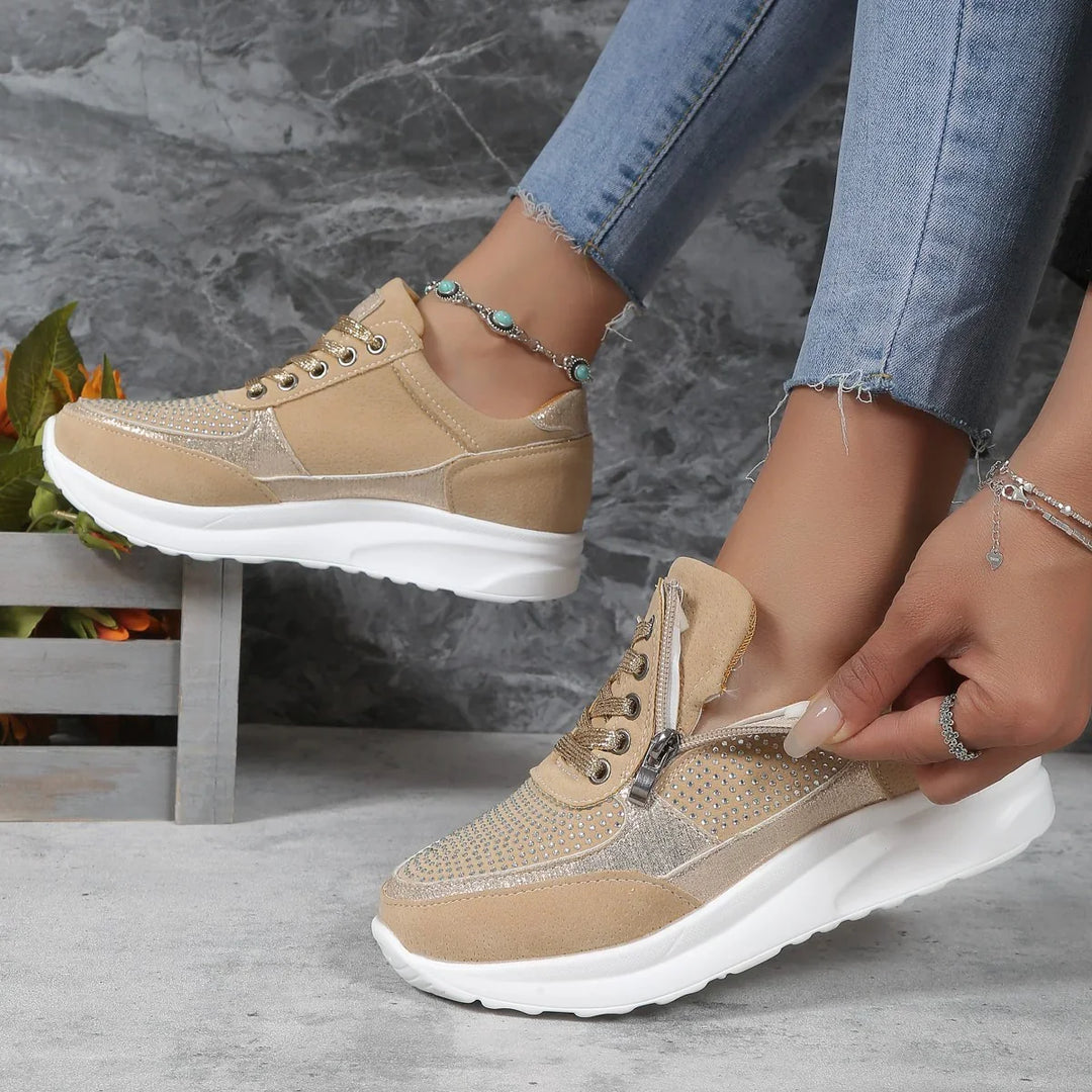 Beige suede sneakers with rhinestones and zipper detail worn with frayed hem jeans against gray background