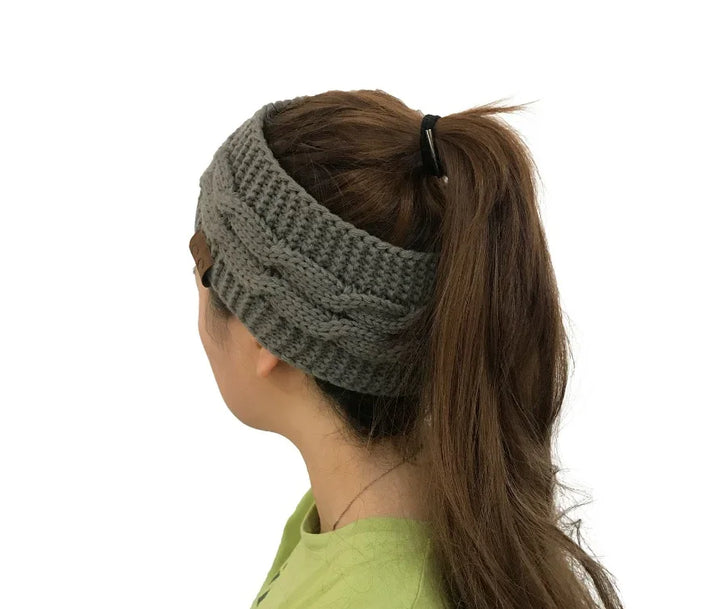 Woman with long brown hair in ponytail wearing gray knitted cable headband against white background