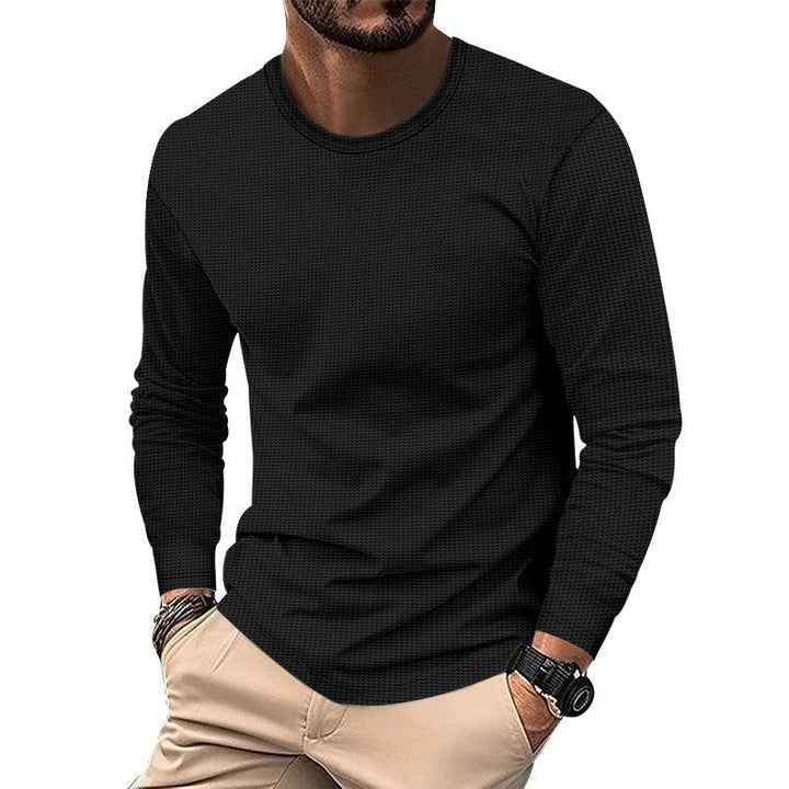 Man wearing black long-sleeve textured shirt with beige pants and wristwatch on white background