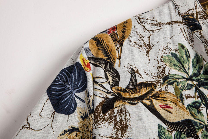 Close-up of fabric with tropical floral print featuring large leaves and flowers in blue, yellow, green, and brown tones on white background