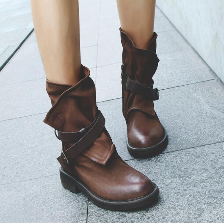 brown leather ankle boots with buckle straps worn on paved outdoor surface