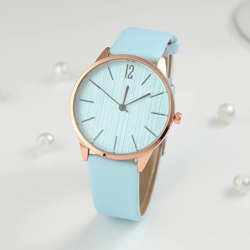 Elegant wristwatch with light blue leather strap and rose gold case on white background with pearls