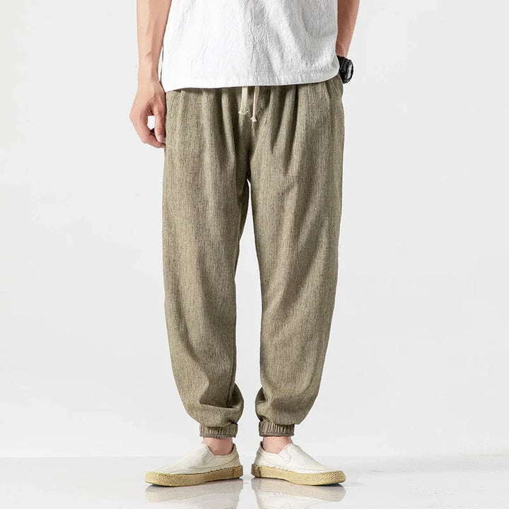 Men's casual beige linen drawstring pants with elastic cuffs paired with white slip-on shoes
