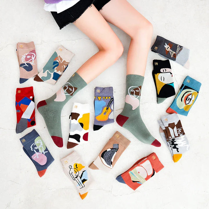 Person wearing green artistic patterned socks surrounded by various colorful abstract art socks on a white floor