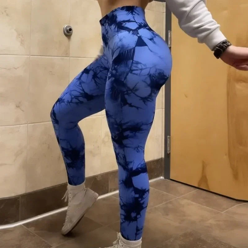 Person wearing blue and black tie-dye high-waisted leggings and white sneakers in a tiled room