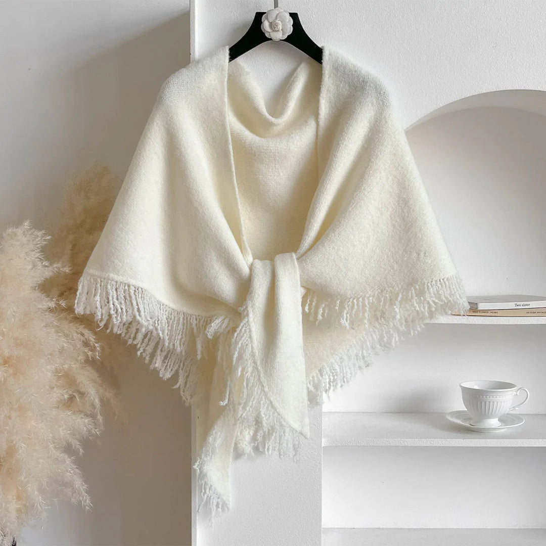 Soft white knitted shawl with fringes hanging on black hanger in minimalist setting