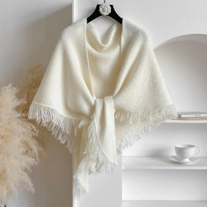 Soft white knitted shawl with fringes hanging on black hanger in minimalist setting