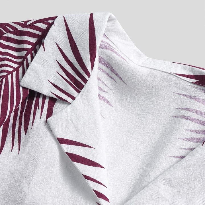 Close-up of a white fabric with maroon tropical leaf print and a folded collar detail