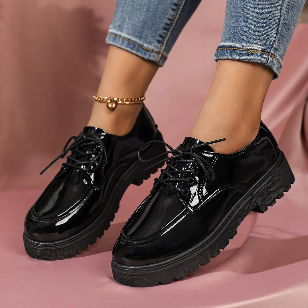 Shiny black patent leather lace-up platform shoes worn with rolled-up jeans and gold heart anklet