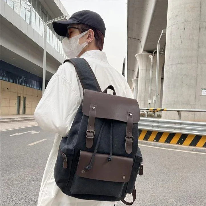 Person wearing white jacket, black cap, face mask, carrying black and brown leather backpack on city street