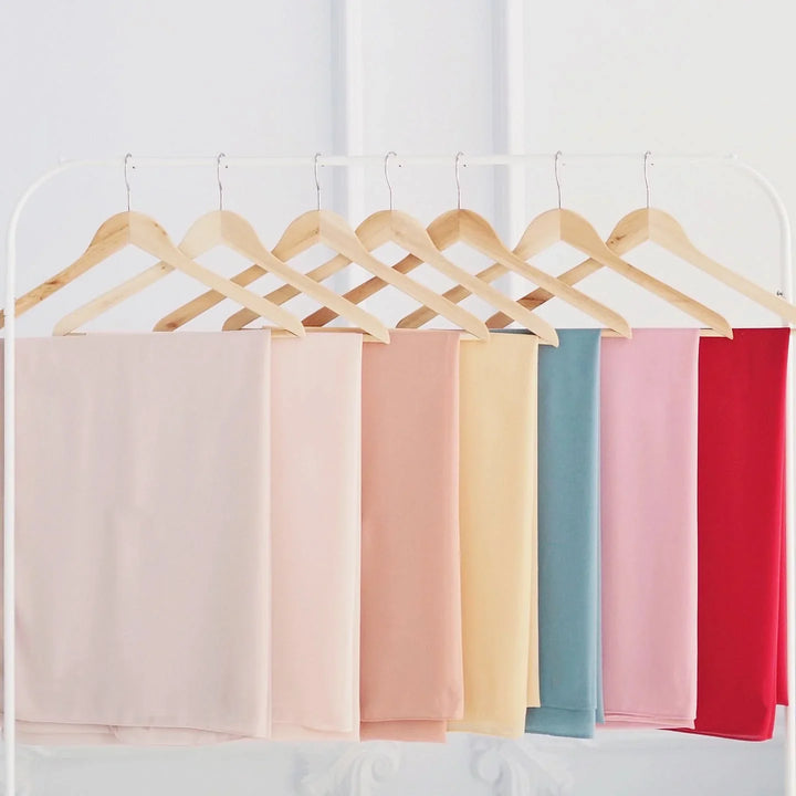 Colorful pastel fabrics hanging on wooden hangers on white clothing rack