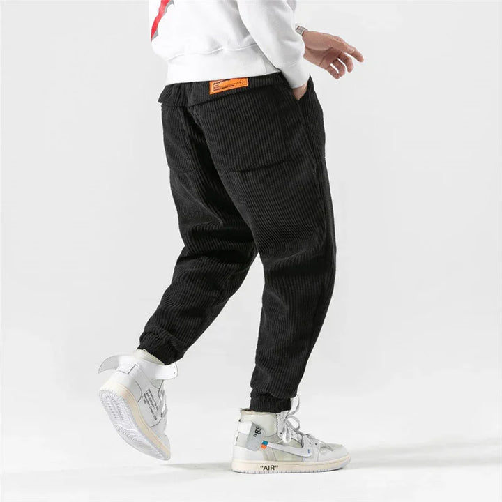 Person wearing black corduroy jogger pants and white high-top sneakers against white background