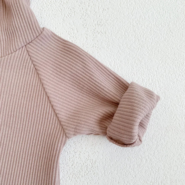 Mauve ribbed knit sweater sleeve with folded cuff on textured white wall