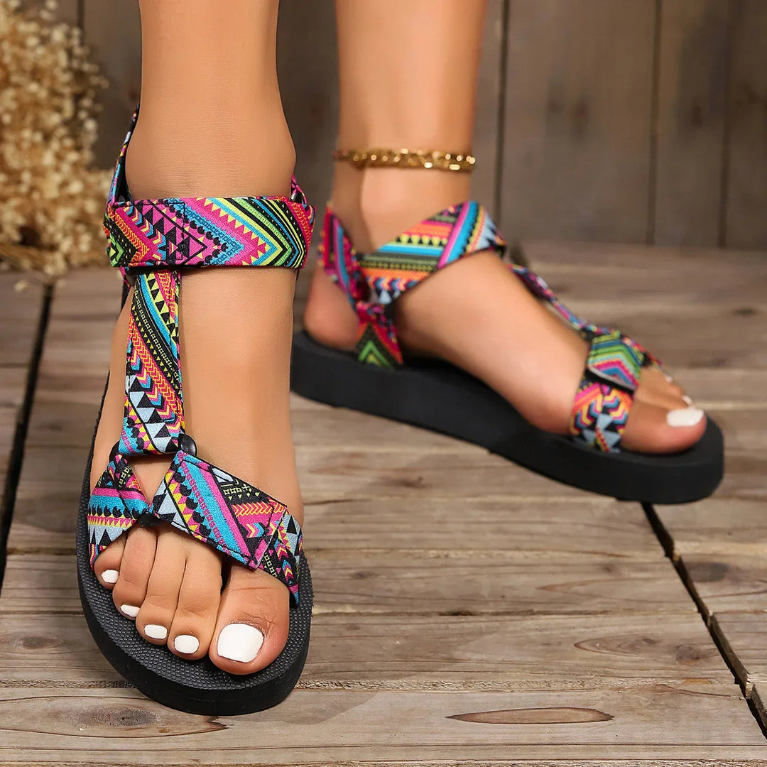 Close-up of feet wearing colorful patterned strap sandals with black soles on wooden floor