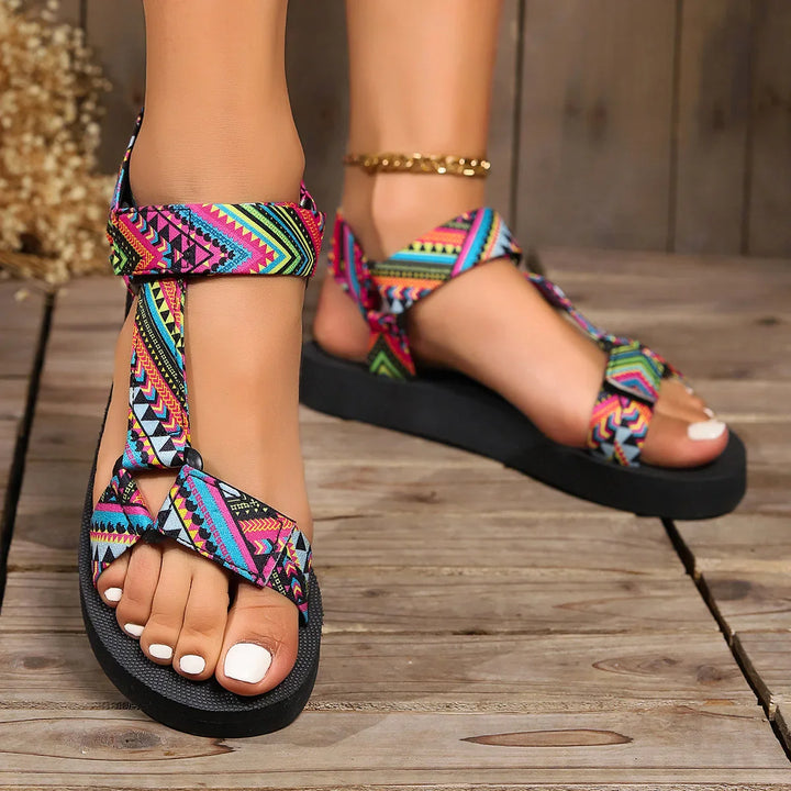Close-up of feet wearing colorful patterned strap sandals with black soles on wooden floor
