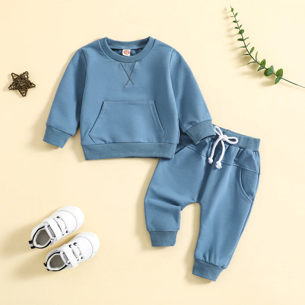 Blue toddler sweatshirt and jogger set with white sneakers on beige background
