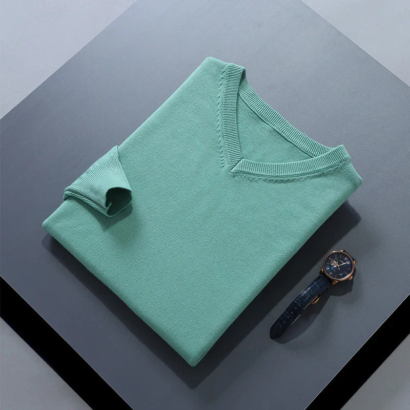 Folded mint green V-neck sweater on dark gray surface beside blue leather wristwatch