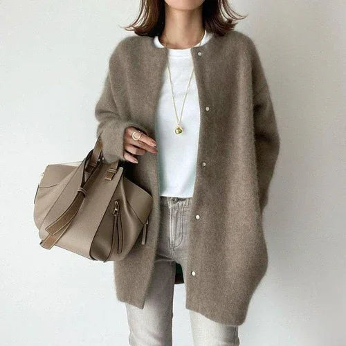 Woman wearing cozy brown buttoned wool cardigan, white t-shirt, gray pants, and carrying taupe leather handbag