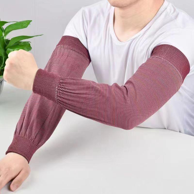 Person wearing red striped protective arm sleeves over a white shirt on a white surface with green plant